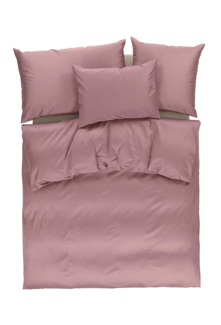 Ein ordentlich gemachtes Bett mit einem lila-rosa Bettbezug und drei passenden Kissen, von oben betrachtet auf weißem Hintergrund.