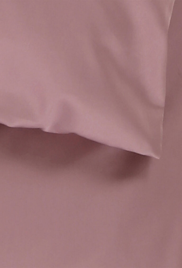 Eine Nahaufnahme eines lilafarbenen Kissens und eines dazu passenden Bettlakens, das eine glatte und weiche Stoffstruktur aufweist.