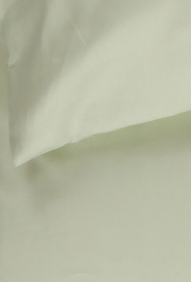 Nahaufnahme eines hellen, cremefarbenen Kissens und Bettlakens, das glatte, weiche und faltenarme Stoffe zeigt.