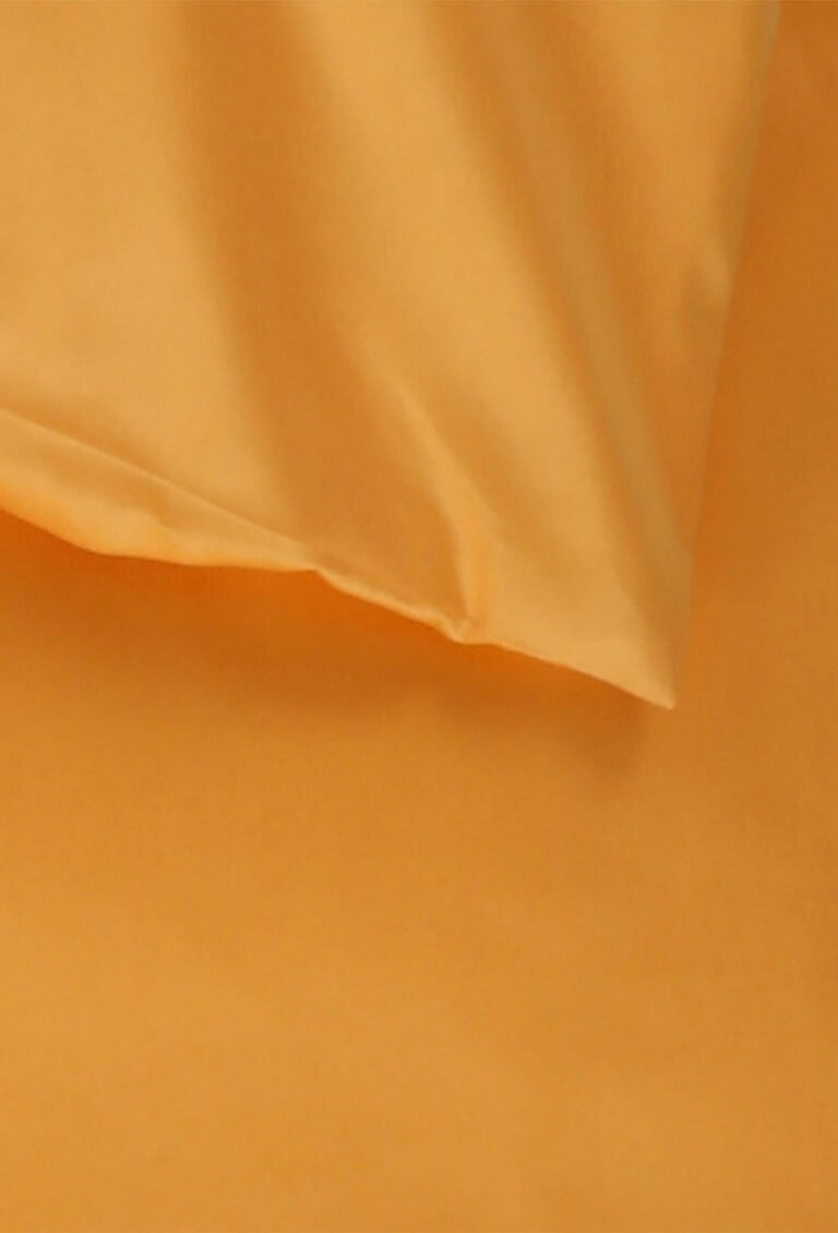 Eine Nahaufnahme eines ordentlich gefalteten orangefarbenen Bettlakens und eines Kissenbezugs aus glattem Stoff vor einem orangefarbenen Hintergrund.