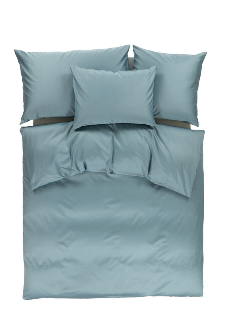 Ein ordentlich gemachtes Bett mit hellblauem Bettzeug, einschließlich eines Bettbezugs, zwei großen Kissen oben und zwei kleineren, symmetrisch angeordneten Kissen, von oben gesehen auf weißem Hintergrund.