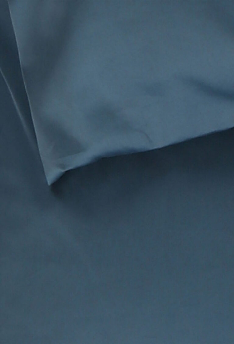 Nahaufnahme eines dunkelblauen Stoffes mit einer teilweise gefalteten Kante, die über eine andere glatte, flache Oberfläche gelegt wurde.