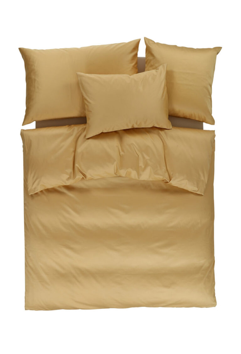 Ein ordentlich gemachtes Bett mit goldgelber Bettwäsche, darunter ein Bettbezug, zwei normale Kissen und ein kleineres Kissen, alles vor einem weißen Hintergrund.