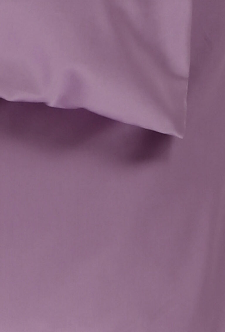 Nahaufnahme eines lavendelfarbenen Bettlakens und eines Kopfkissenbezugs, beide aus glattem Stoff. Das Kopfkissen befindet sich im oberen Teil des Bildes und hebt sich teilweise von dem passenden Laken ab.