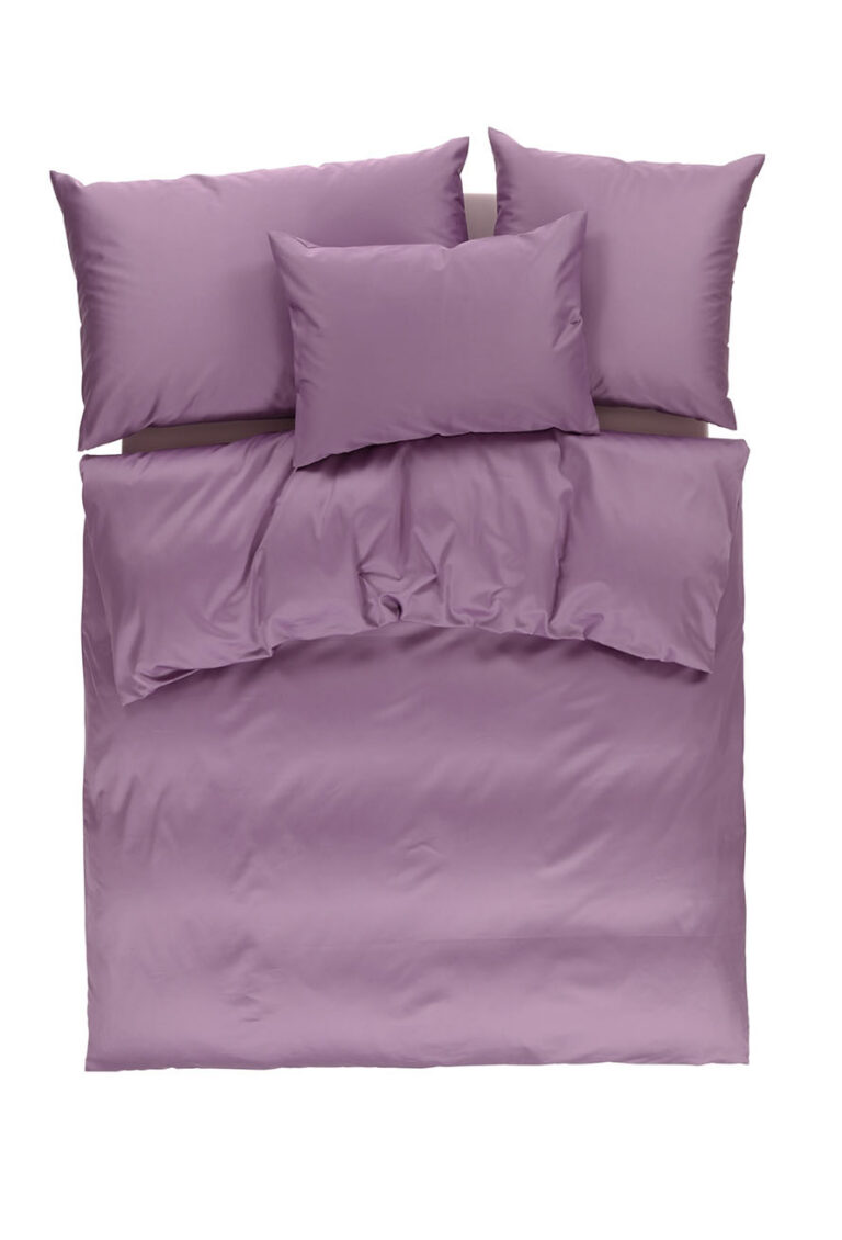 Ein ordentlich gemachtes Bett mit einem malven- oder lavendelfarbenen Bettbezug und Kissenbezügen, darunter drei große Kissen und ein kleineres Kissen, von oben gesehen auf weißem Hintergrund.