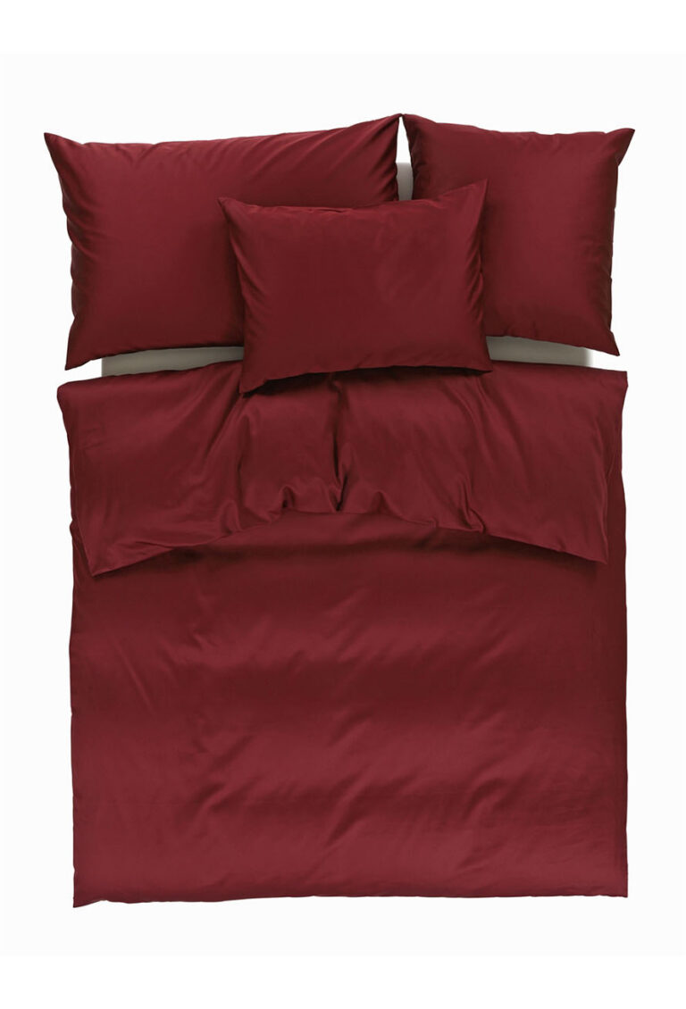 Ein ordentlich gemachtes Bett mit tiefroter Bettwäsche, einschließlich einer Bettdecke, zwei großen Kissen am Kopfende und einem kleineren Kissen in der Mitte, von oben gesehen vor einem weißen Hintergrund.
