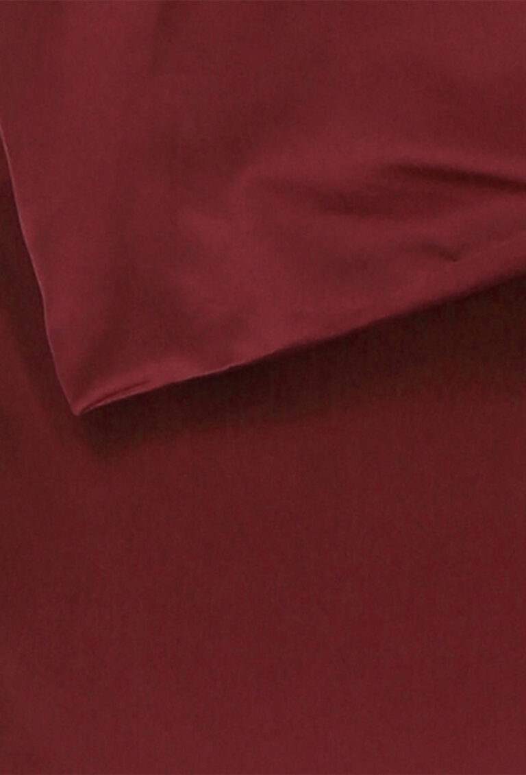 Nahaufnahme eines glatten, weinroten Stoffes, möglicherweise eines Bettlakens und eines Kissenbezugs, der seine weiche Textur und seine satte, kräftige Farbe zeigt.