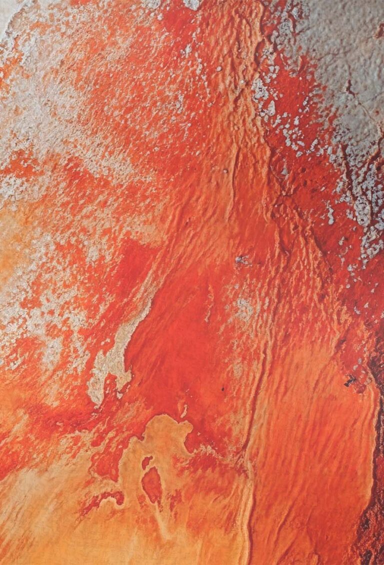 Nahaufnahme einer strukturierten Oberfläche mit roten, orangen und weißen Farbtönen, die an eine raue, verwitterte Wand oder abstrakte Kunst mit verschiedenen Farbtönen und unregelmäßigen Mustern erinnert.