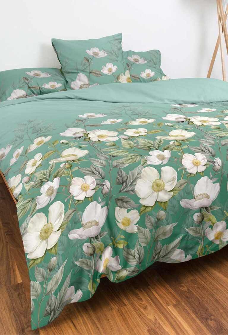 Ein ordentlich gemachtes Bett mit grüner Bettwäsche mit weißem und gelbem Blumenmuster, passenden Kissenbezügen und einem Holzboden.