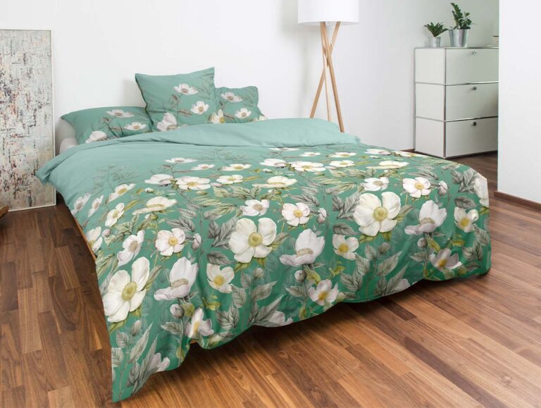 Ein ordentlich gemachtes Bett mit grüner Blumenbettwäsche und Kissen in einem hellen Zimmer mit Holzboden, einer weißen Stehlampe, Topfpflanzen und einer weißen Kommode neben dem Bett.