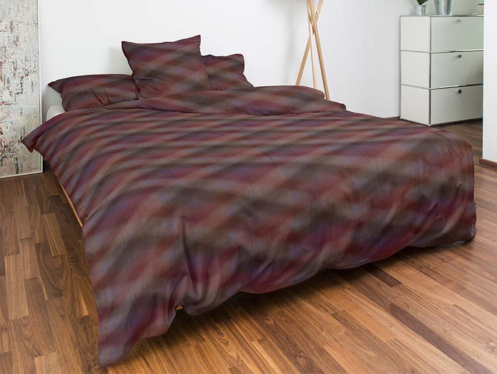 Ein ordentlich gemachtes Bett mit einer dunklen, bunt gemusterten Bettdecke und Kissen, in einem modernen Schlafzimmer mit Holzfußboden, weißen Wänden, einer Kommode und einer Stehlampe.